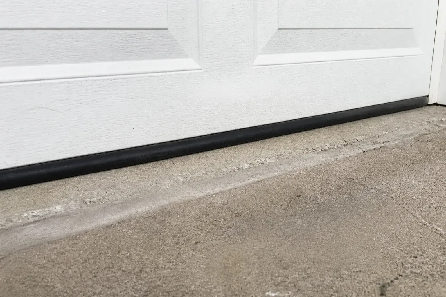 Black bottom seal along a closed white garage door at a concrete threshold. — Garage Door Bottom Seal Replacement, Mount Albert