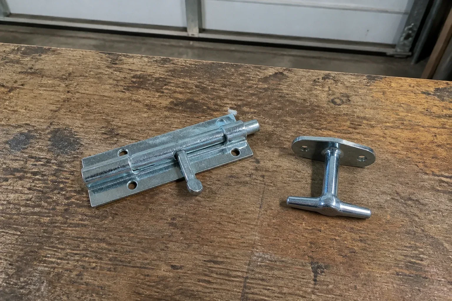 Detached slide bolt and T-handle on a wooden garage workbench. — Garage Door Manual Lock Repair, Mount Albert